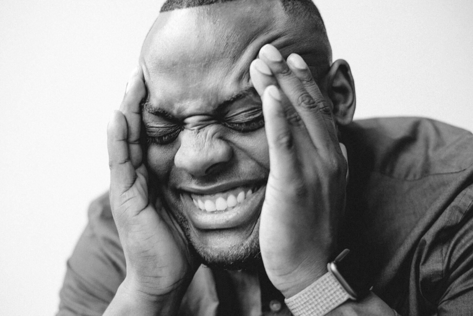 Black and white close-up of a joyful man with hands on his head, eyes closed.